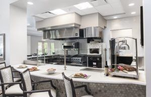 A modern industrial kitchen with stainless steel appliances and a bar counter with seating.