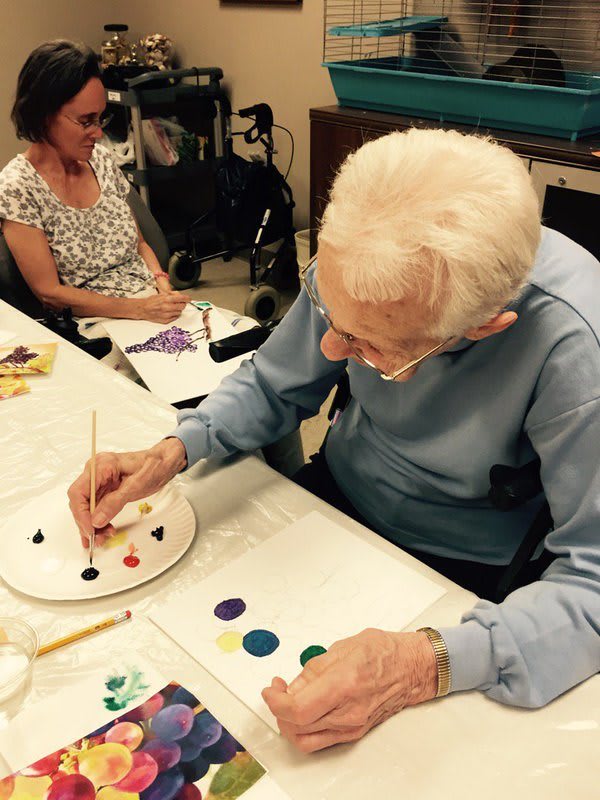 An elderly person painting at a table during an indoor art activity.
