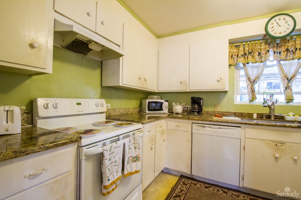 A cozy kitchen with white cabinets and green walls, featuring modern appliances including an oven, microwave, coffee maker, and dishwasher.