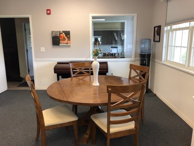 A cozy dining area with a round wooden table and chairs, featuring a decorative vase in an office setting.