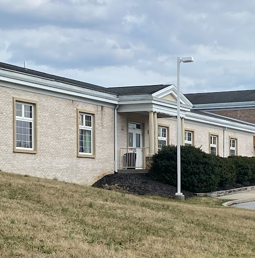 A view of a modest commercial or institutional building set against a grassy landscape under a cloudy sky.
