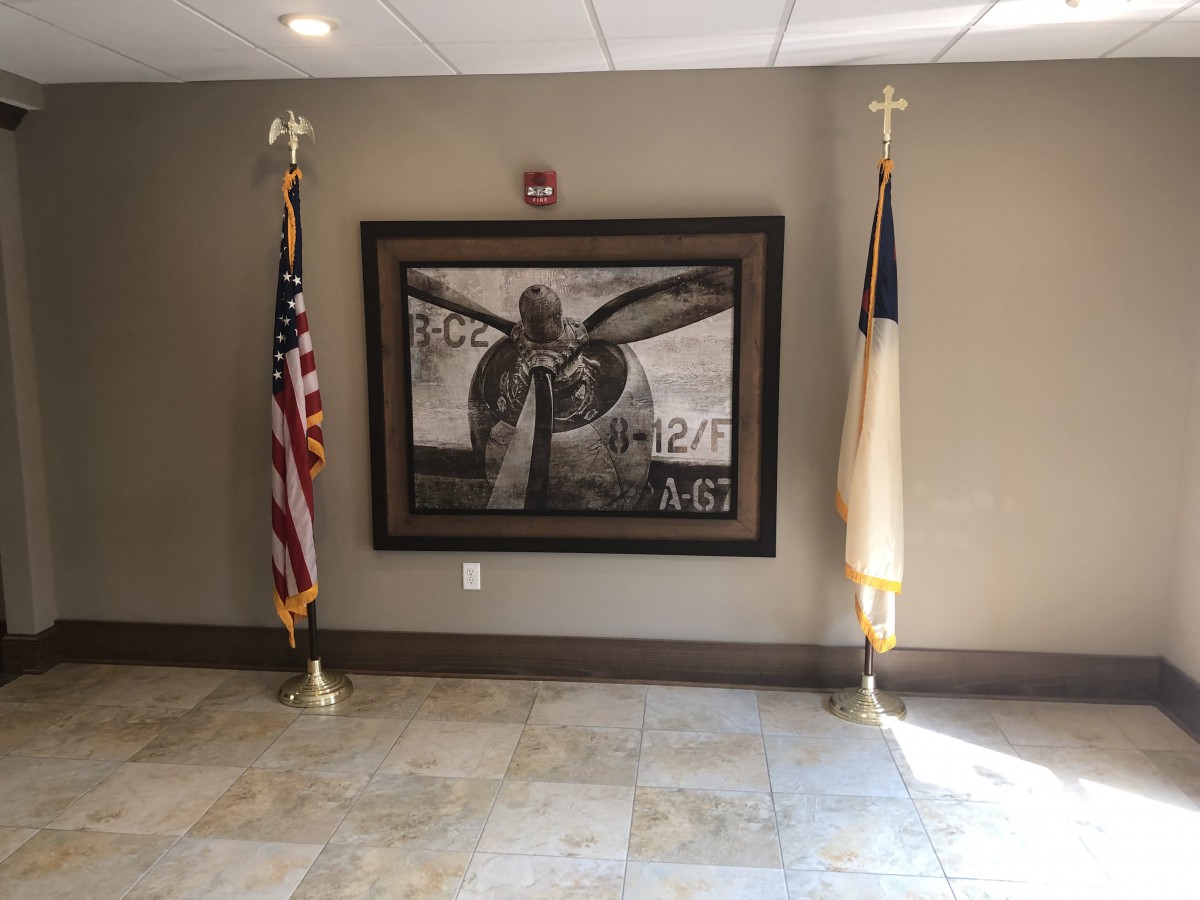 This image shows an interior wall with a prominent painting flanked by an American flag and a church flag.