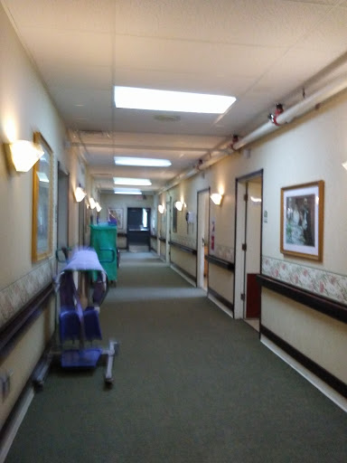 A well-lit hallway in a healthcare facility, featuring doors and framed artwork along the walls.