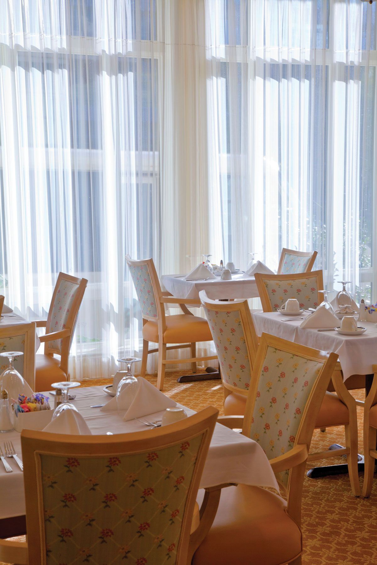 A bright and elegant restaurant interior with neatly arranged tables and chairs by large windows.
