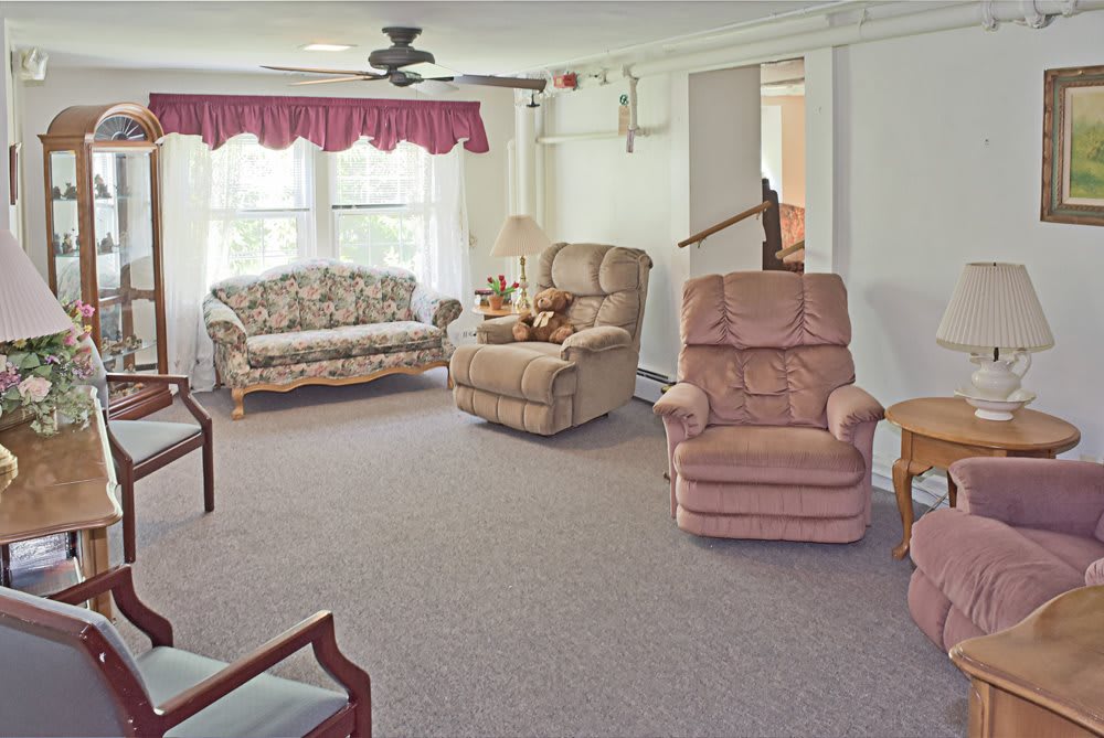 A cozy living room featuring a floral sofa, two plush armchairs, and bright natural lighting from a large window.