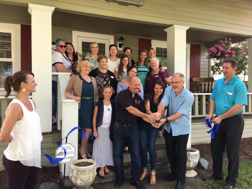 A group of people gathered on a porch for a ribbon-cutting ceremony.