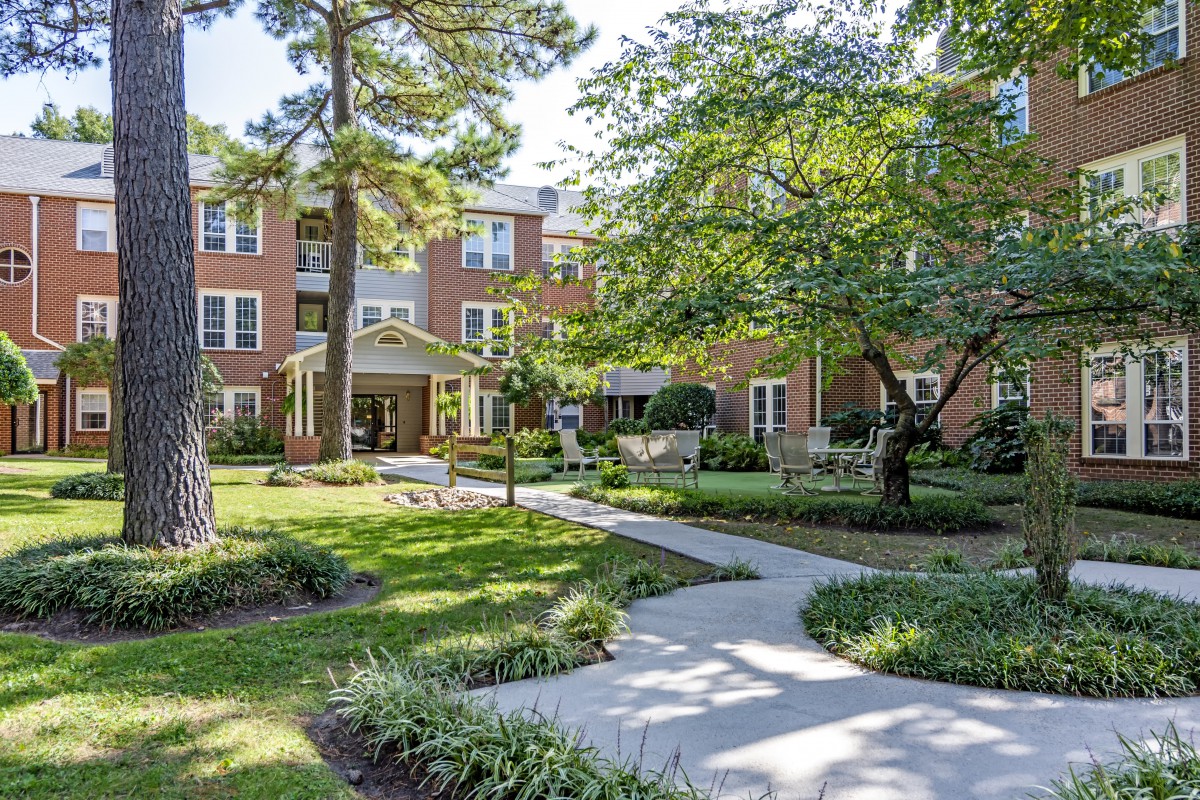 A scenic view of a brick residential building surrounded by lush greenery and a paved pathway.