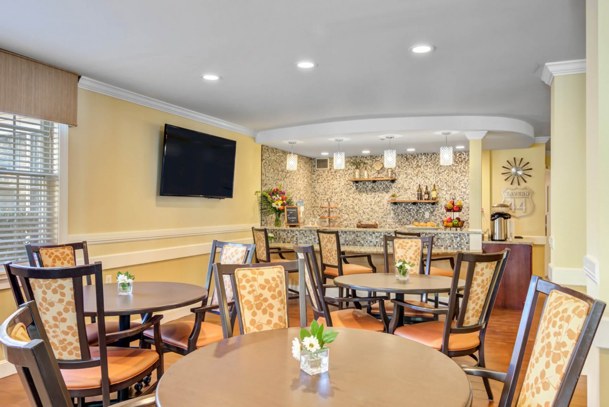 A cozy dining area with round tables and chairs, featuring a mounted television and stylish lighting.