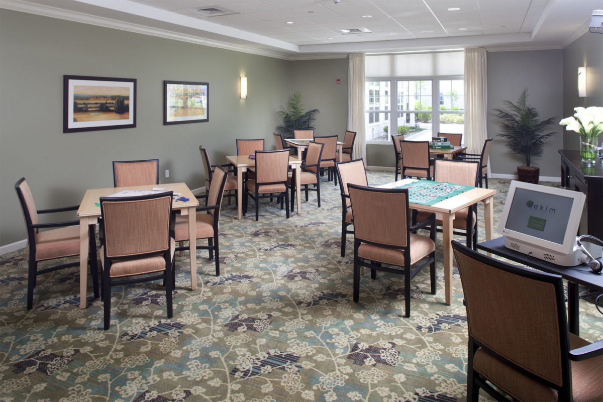 A well-lit dining area with multiple tables and chairs, featuring a patterned carpet and large windows.