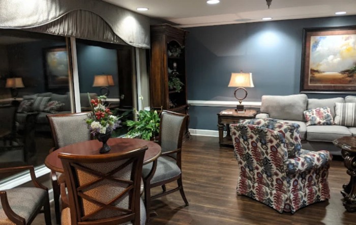 A cozy living room with elegant furniture and soft lighting, featuring a floral sofa and wooden flooring.
