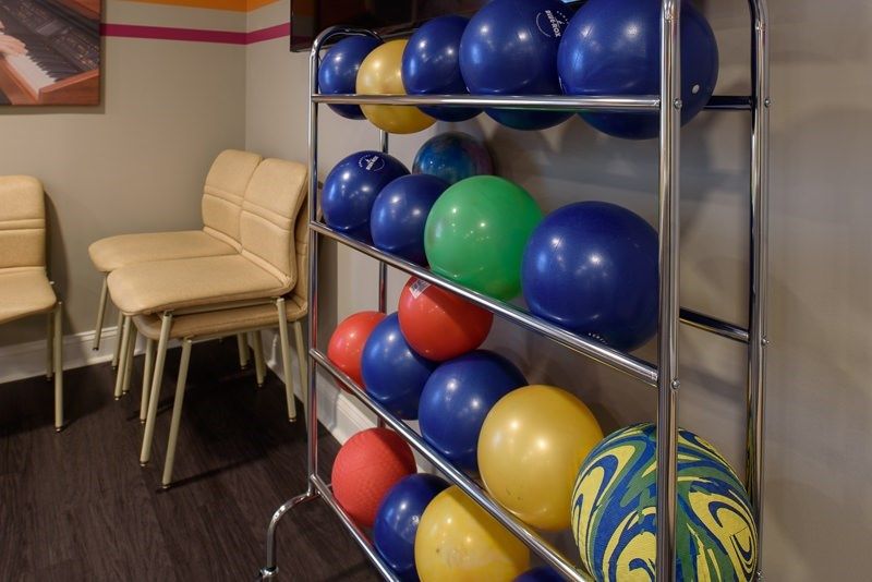 A rack filled with colorful bowling balls next to a set of chairs in an indoor setting.
