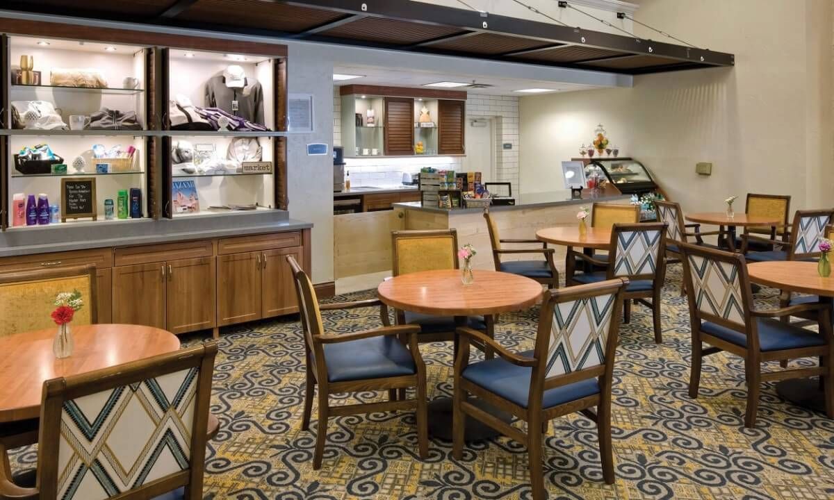A cozy cafe interior with tables and chairs arranged on a patterned carpet.