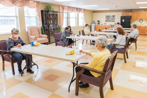 A group of senior citizens seated at tables in a community center, engaging in activities.