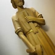 A wooden statue of a standing figure holding a long object.