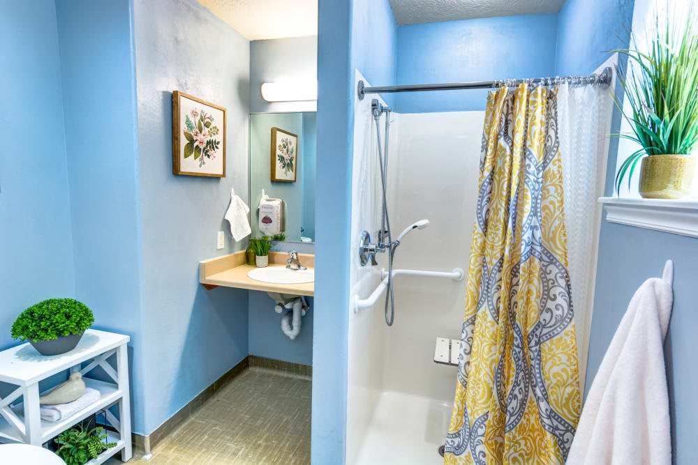 A bright bathroom with blue walls, featuring a shower with a yellow curtain and an accessible sink area.