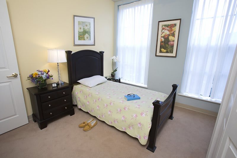 A cozy bedroom featuring a single bed, a nightstand with a lamp, and decorative art on the walls.