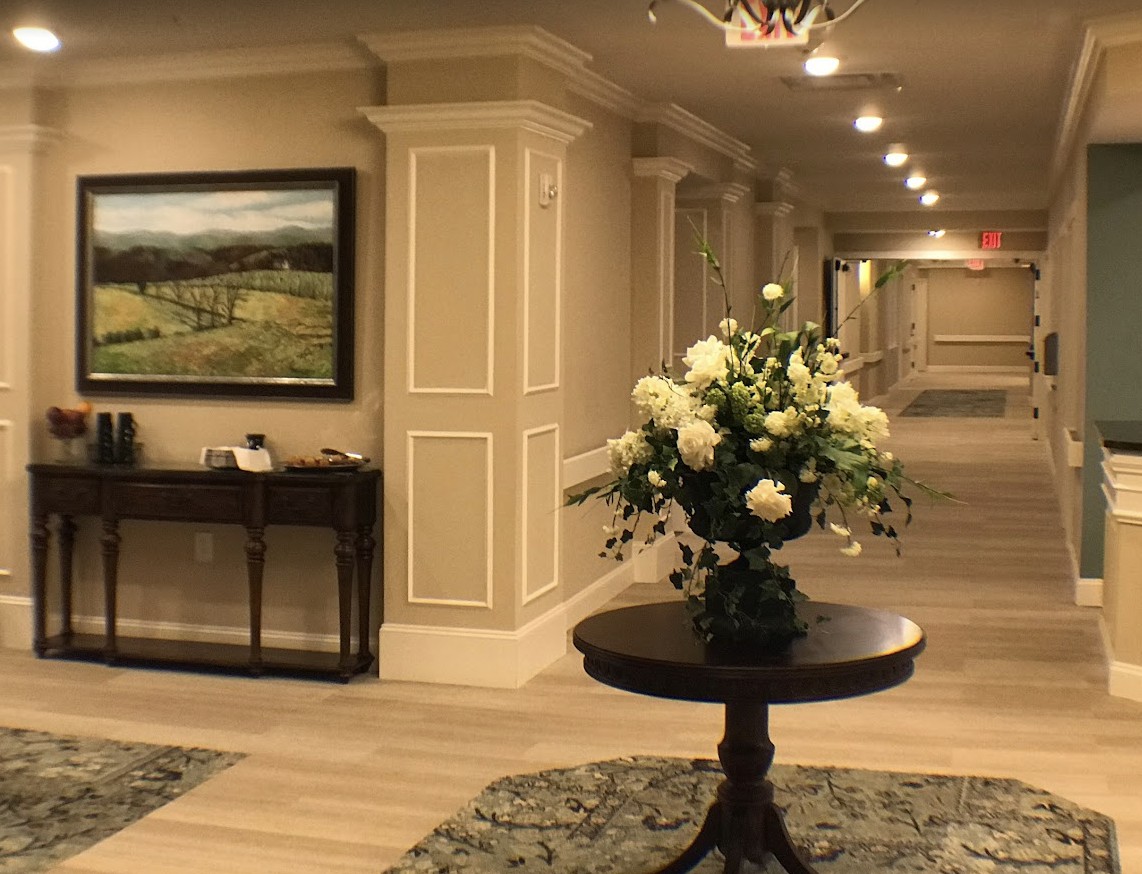 A hotel lobby with elegant interior design, featuring a round table adorned with flowers and a framed landscape painting on the wall.