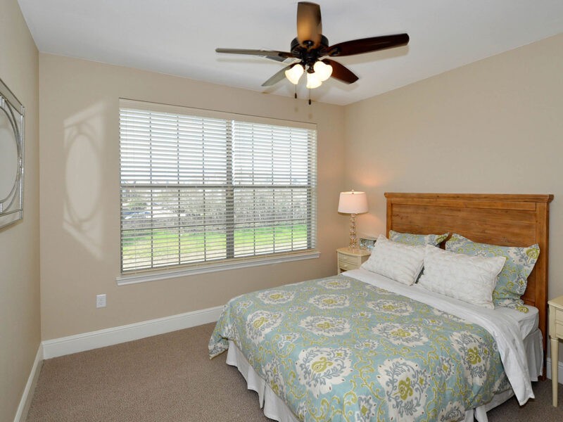 A cozy bedroom with a large window, ceiling fan, and neatly made bed.