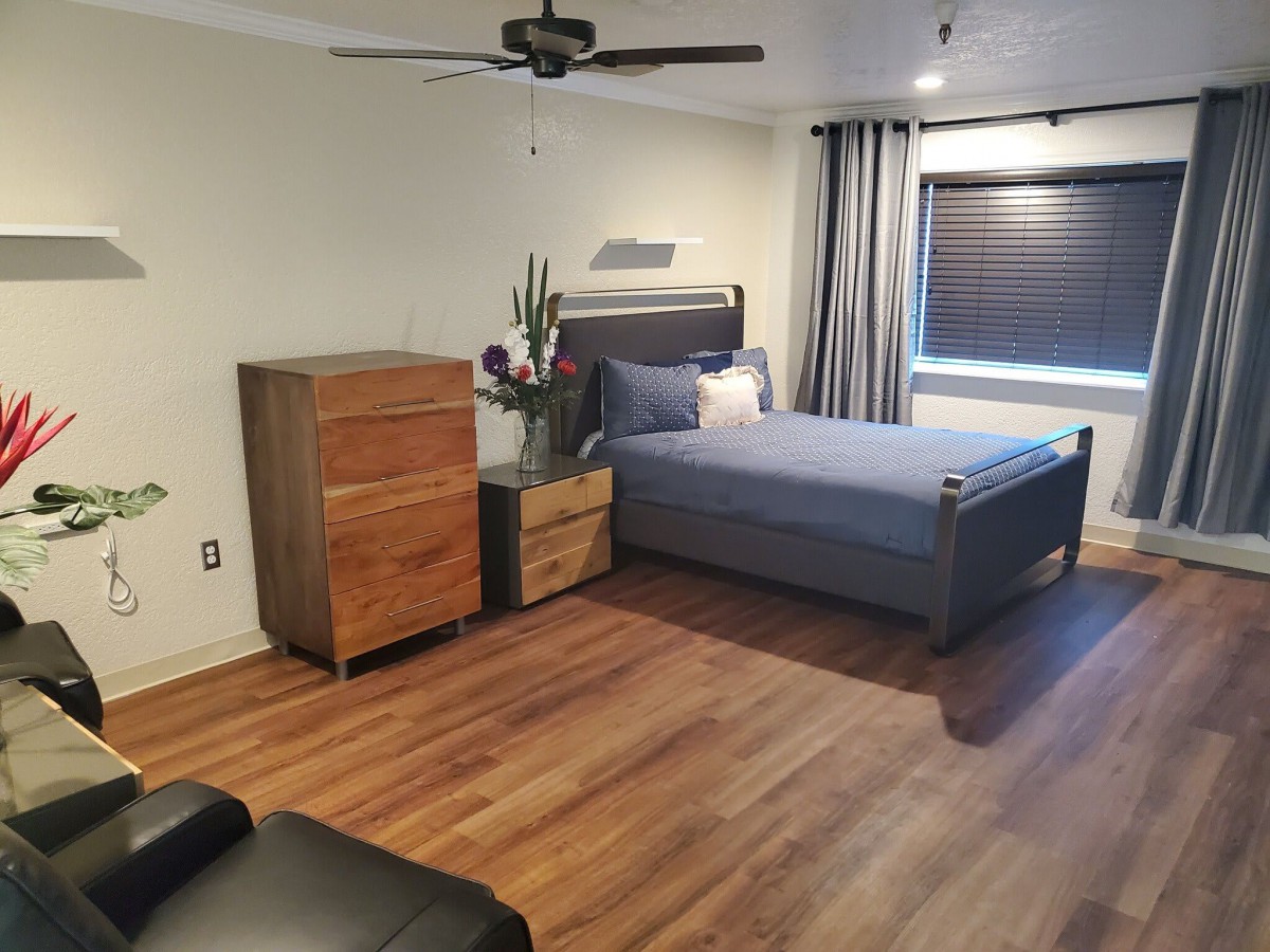 A modern minimalist bedroom with a wooden floor, featuring a bed and dresser.