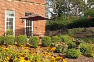 A beautifully landscaped garden with vibrant flowers and a cozy patio outside a brick building.