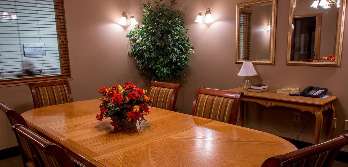 A cozy dining room with a wooden table, striped chairs, and decorative elements including flowers and a lamp.