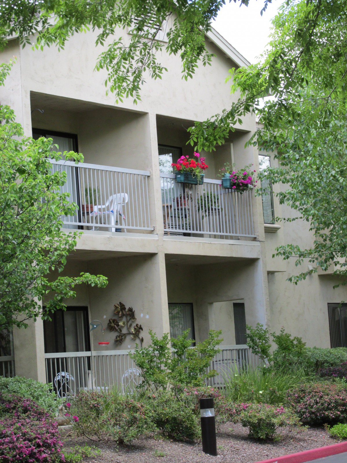 A view of an apartment building with balconies adorned with plants and surrounded by greenery.