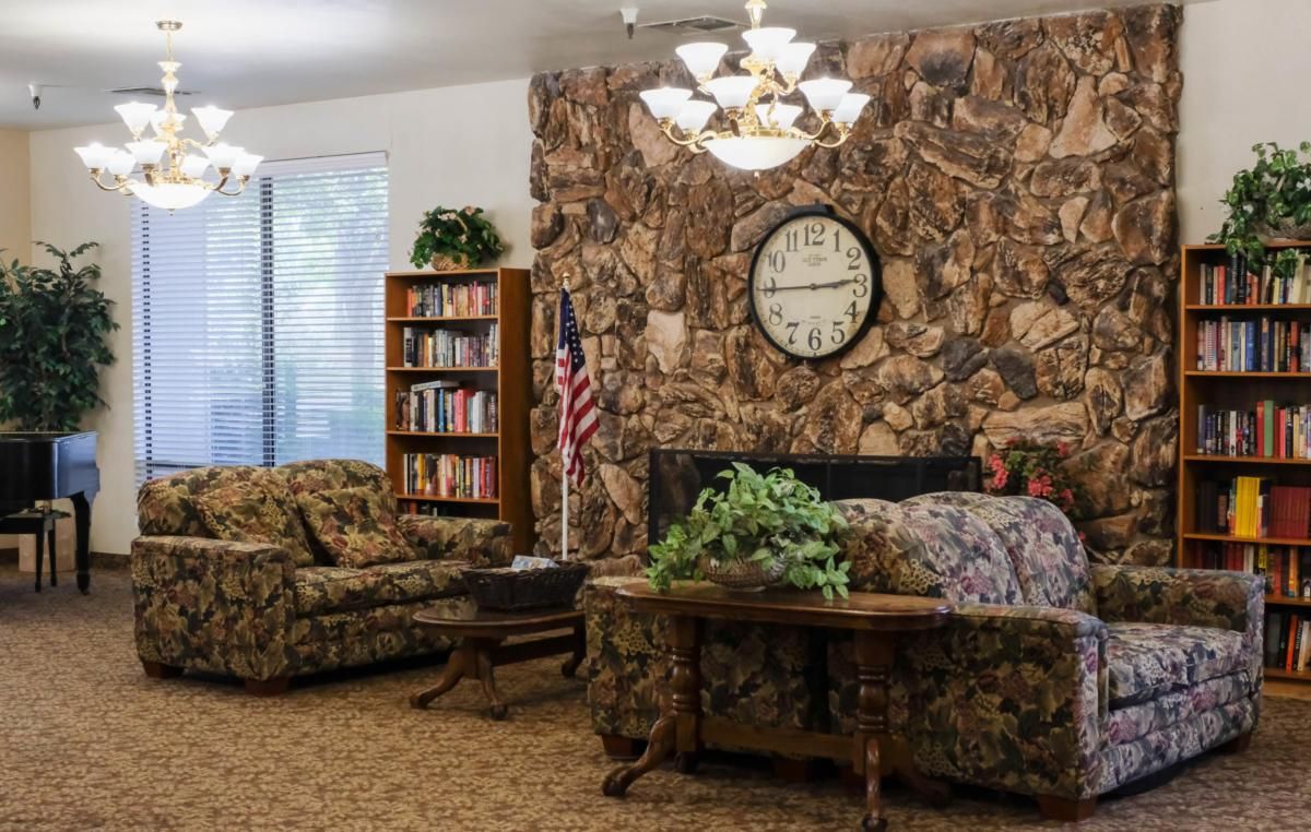 A cozy living room with a stone wall, featuring a bookshelf, clock, and furniture.