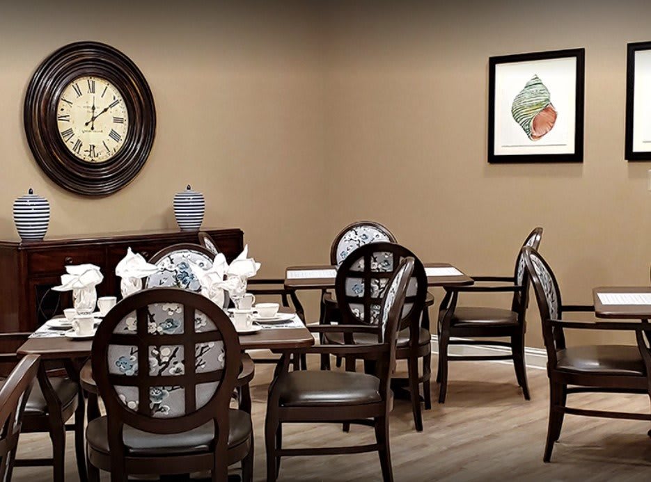 A dining room with a set of elegant wooden chairs and table, featuring a wall clock and artwork.