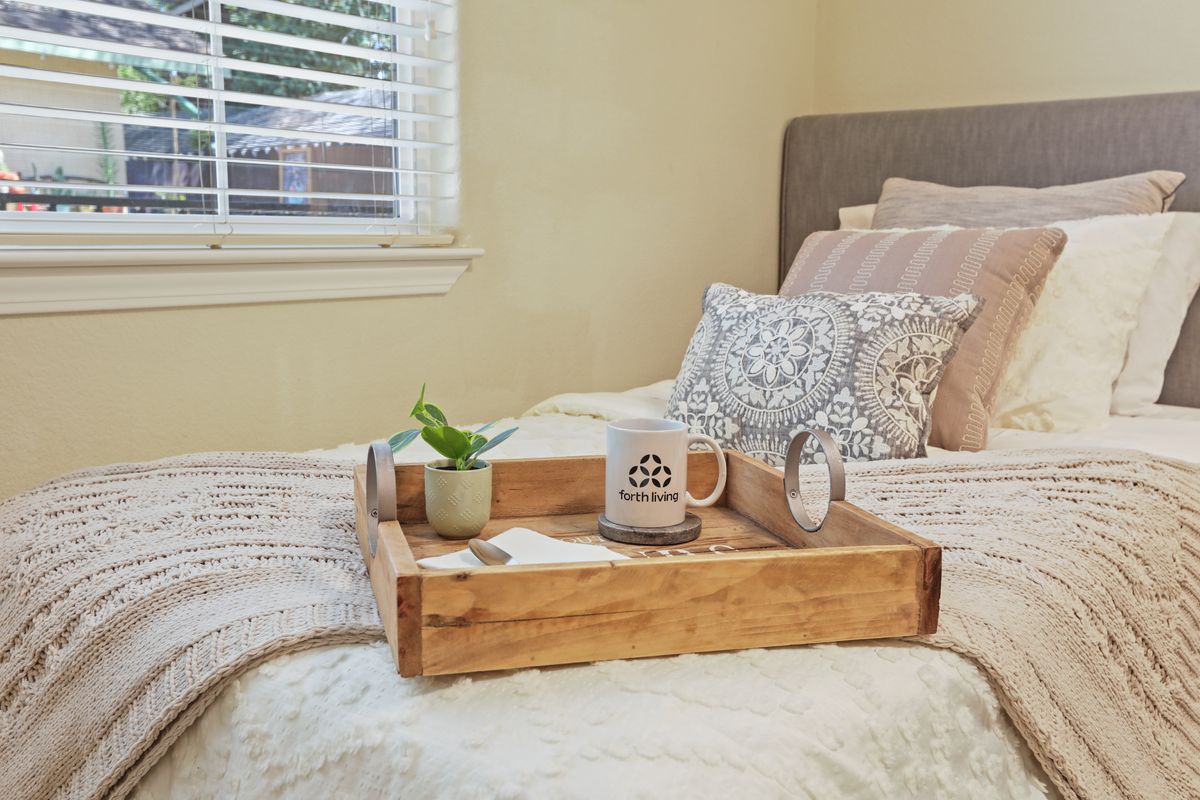 A cozy bedroom scene with a breakfast tray on the bed featuring a mug, small plant, and decorative items.