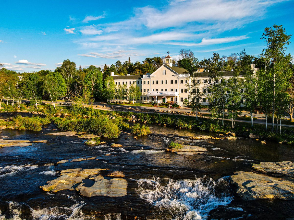 A scenic view of a river cascading over rocks with a picturesque building in the background under a clear blue sky.