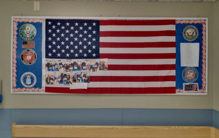 A large American flag displayed on a wall with photos attached to it.
