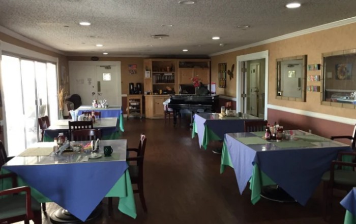An empty restaurant dining area with tables set and covered in blue and green tablecloths.