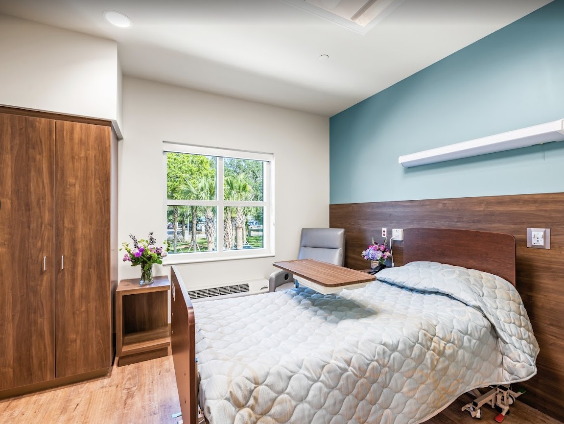 A minimalist hospital room with a single bed, wooden furniture, and a window view.