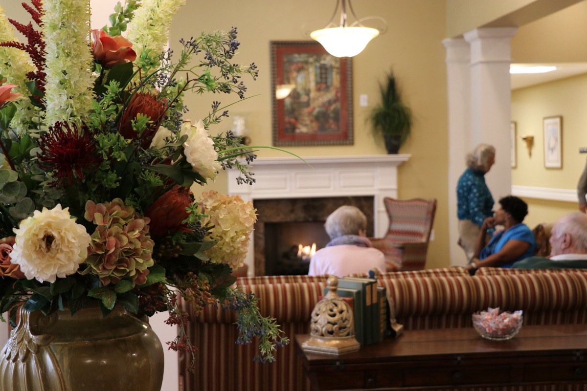 A cozy living room with a flower arrangement and people relaxing near the fireplace.