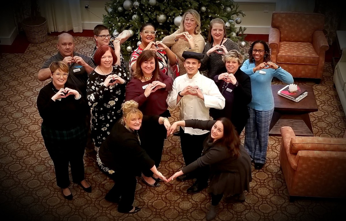 A group of people making heart gestures in front of a decorated Christmas tree.