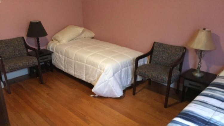 A simple bedroom with a single bed, chair, and nightstand.