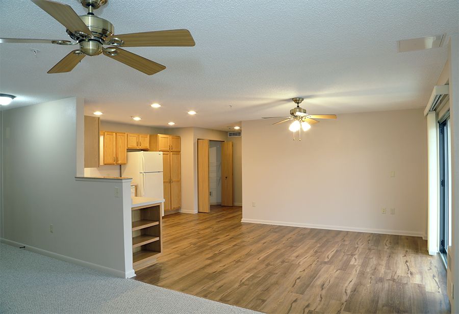 Spacious open-concept living area with wood flooring, ceiling fans, and recessed lighting adjacent to a kitchen.