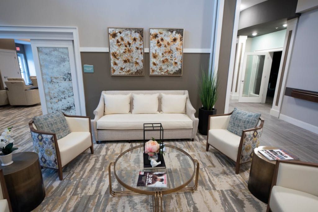 A modern living room with a sofa, two chairs, and a glass coffee table, accented by decorative pillows and wall art.