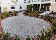 A landscaped garden with a gravel pathway surrounded by greenery and plants.