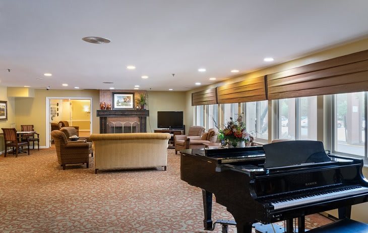 A cozy living room with a grand piano, featuring comfortable seating and a fireplace.