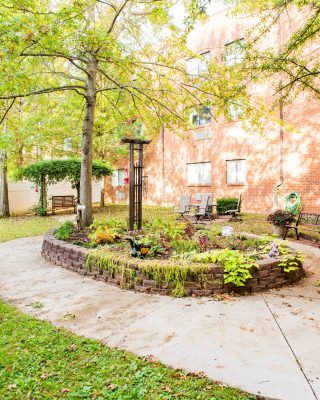A well-maintained garden area with trees and plants, adjacent to a brick building.