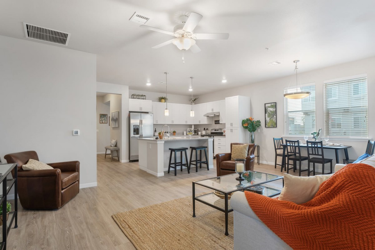 A modern open space living room and kitchen area with neutral tones and bright lighting.