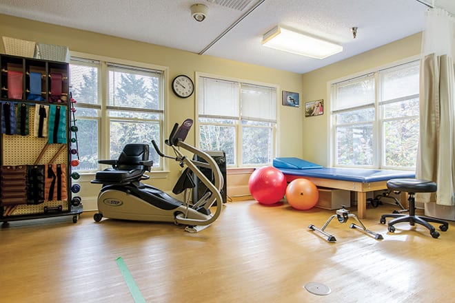 A well-lit therapy room with exercise equipment, including a stationary bike and colorful exercise balls.