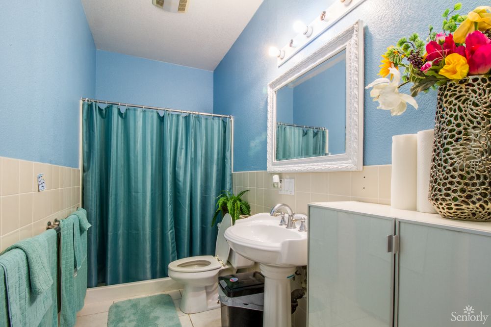 A bright bathroom with blue walls, featuring a white sink, large mirror, and teal shower curtain.