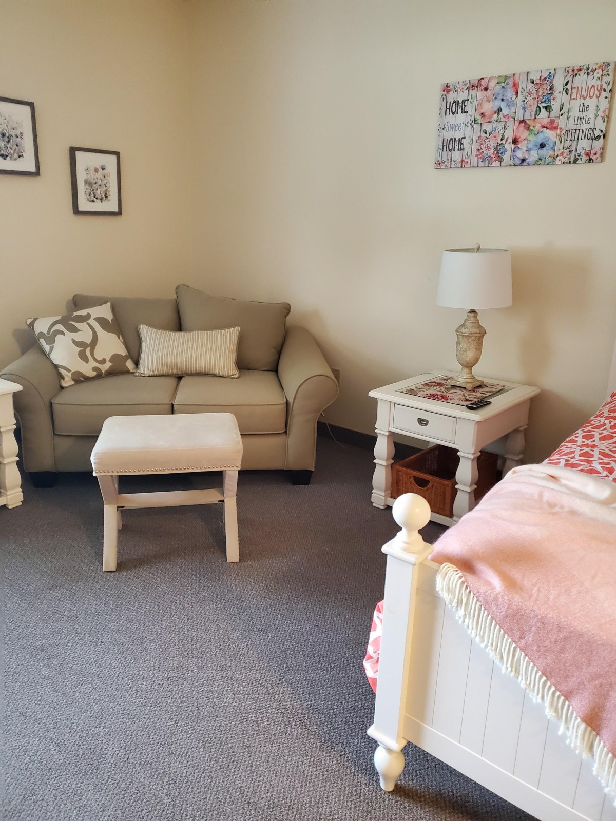 A cozy living room with a sofa, lamp, and small coffee table beside a bed.
