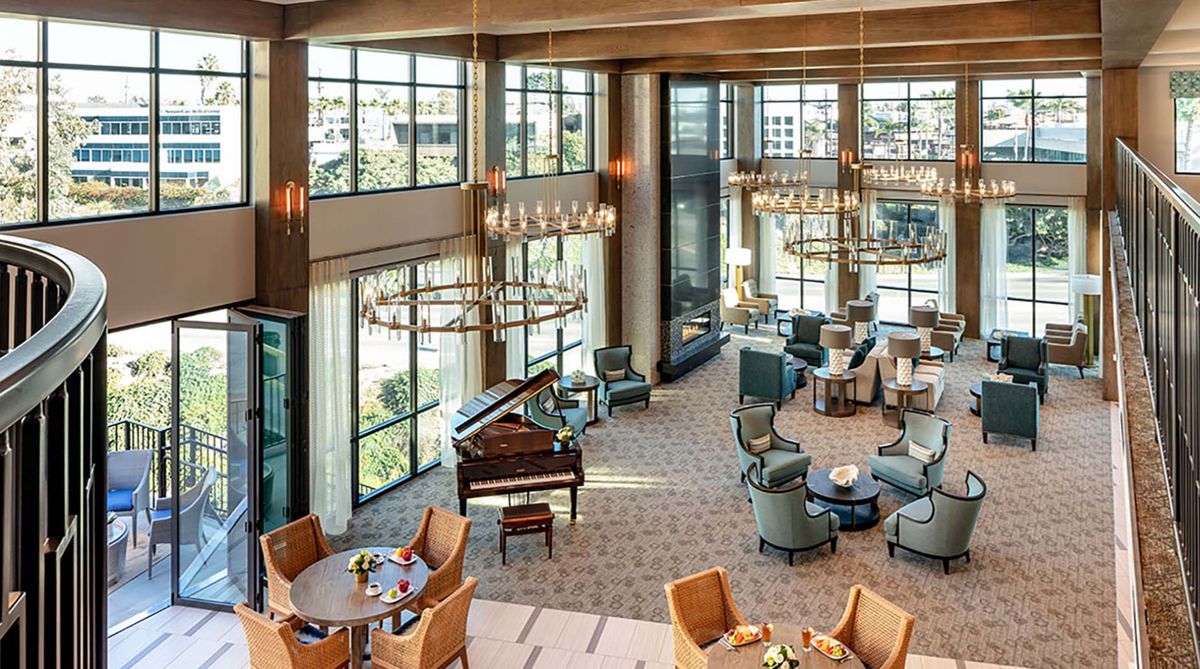 A spacious and elegantly designed lobby featuring multiple seating areas, a grand piano, large windows, and chandeliers.