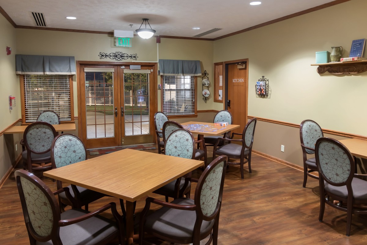 A cozy dining area with wooden tables and chairs, featuring a warm decor and ample natural light from the windows.