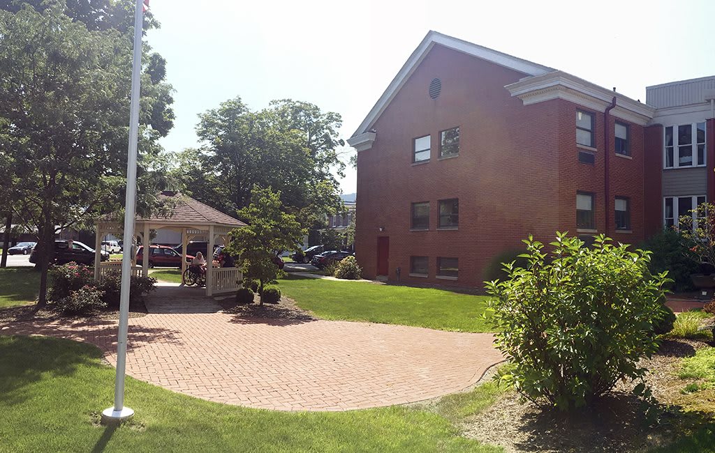 A sunny day view of a brick building with a gazebo and lush green lawn.