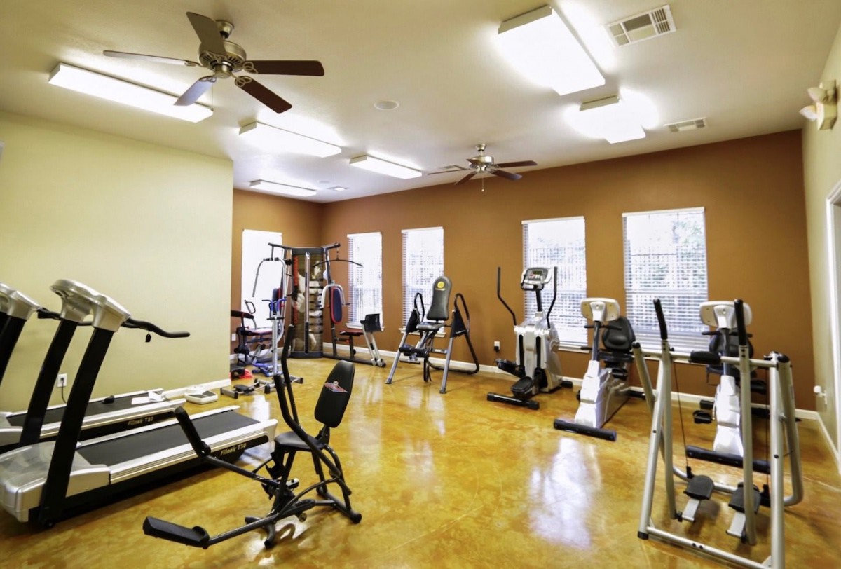 A well-lit gym with various exercise equipment, including treadmills and elliptical machines.