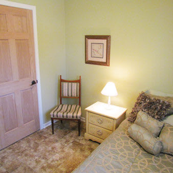 A cozy bedroom with a single bed, nightstand, and chair against green walls.